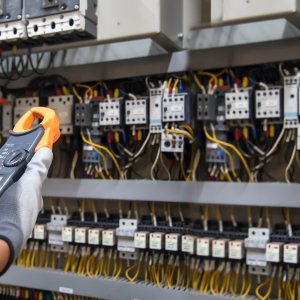Electricity and electrical maintenance service, Engineer hand holding AC voltmeter checking electric current voltage at circuit breaker terminal and cable wiring main power distribution board.