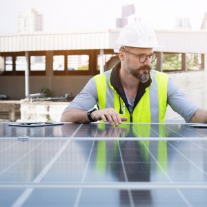 Rooftop solar power plant engineers sitting and examining photovoltaic panels. Concept of alternative energy and its service. Electrical and instrument technician use laptop to maintenance electric