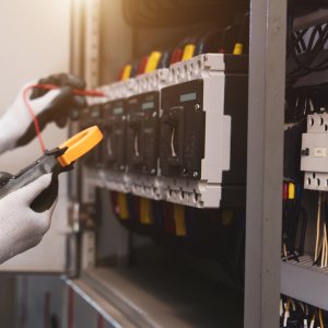 Electrical service technician holding electricity checking equipment to check electric current circuit breaker terminal panel and cable wiring main power distribution board for maintenance system.