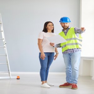Worker and woman customer engage in a discussion, planning a home renovation together. They use a blueprint during the briefing to outline the construction details and collaborate on the process.